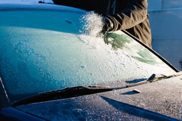 Man defrosts frozen windscreen on cold icy morning