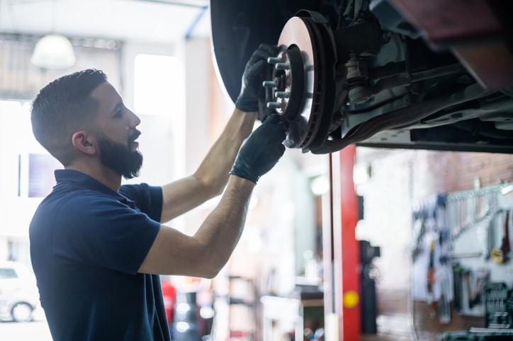 Young mechanic checking the brake disk of a car on lift at the workshop - Car industry concepts