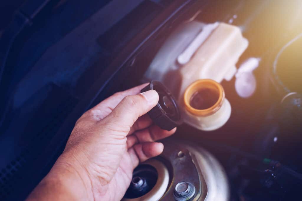 close up of man hand holding cap of brake fluid reservoir tank while checking brake fluid level in an engine