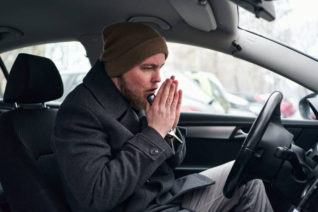 Male sat in driving seat trying to warm hands up by blowing on them