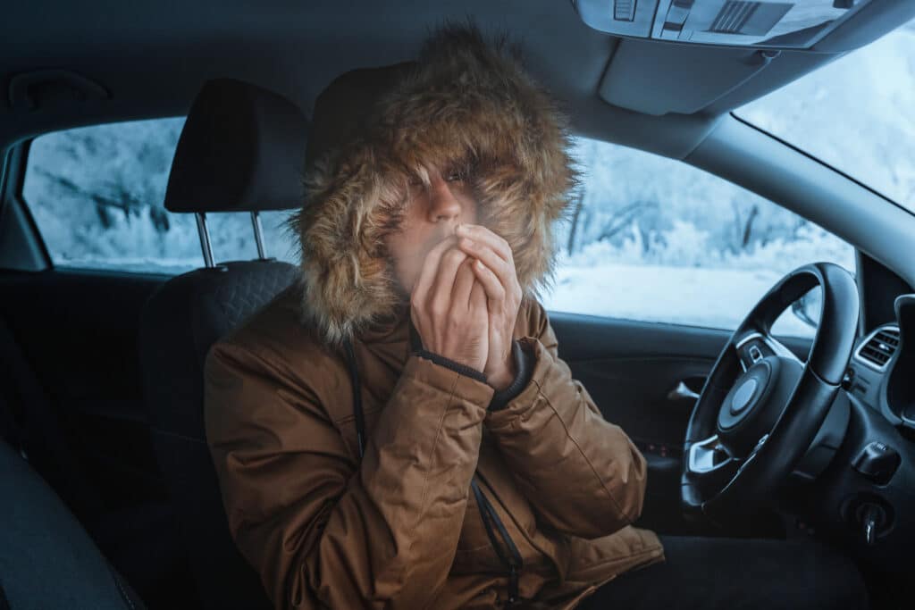 Women wearing thick coat sat at the drivers seat blowing warm air on to her hands