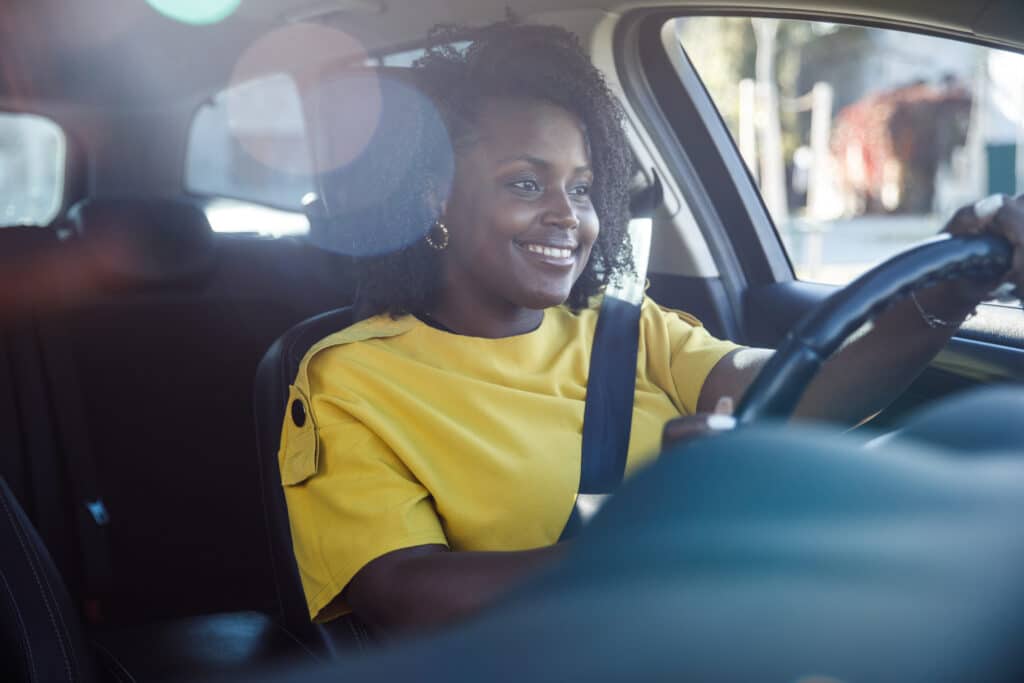 Female wearing bright yellow top smiling whilst driving her car